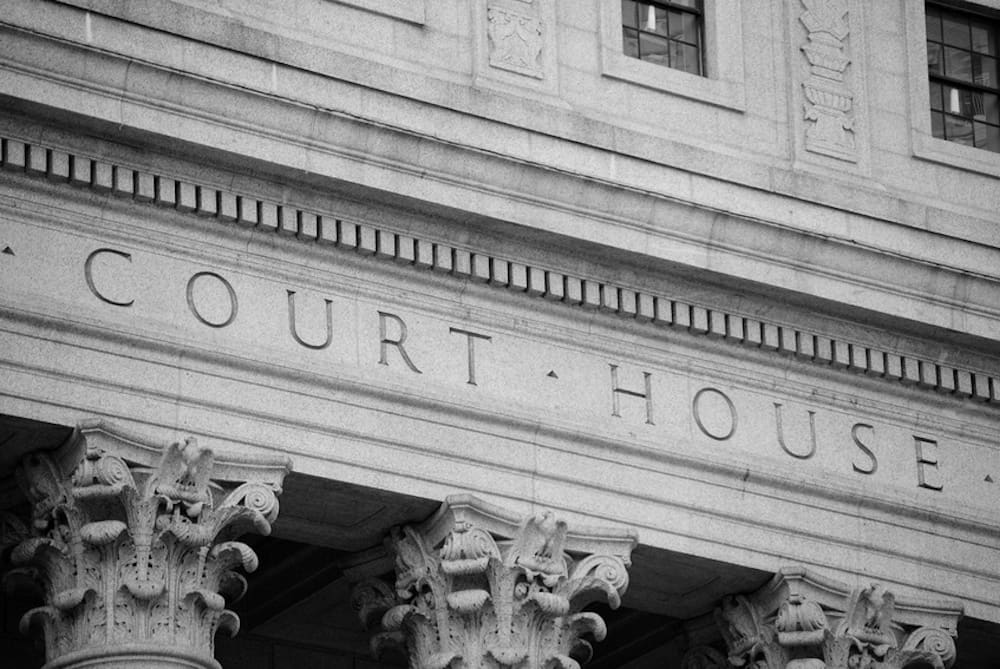 Black and white image of the facade of a courthouse with ornate columns and engraved lettering stating 